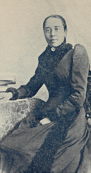 Schwarz-Weiß Foto von Anna Julia Cooper. Sitzend in hochgeschlossenem Kleid. Blick in die Kamera Schwarz-Weiß Foto von Anna Julia Cooper. Sitzend in hochgeschlossenem Kleid. Blick in die Kamera