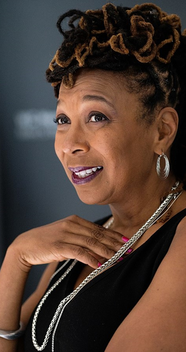 Mohamed Badarne, Kimberlé Crenshaw (40901215153), CC BY-SA 4.0 Kimberly Crenshaw in ärmellosem schwarzen Oberteil mit silberner Kette. Rechte Hand liegt am linken Schlüsselbein. Blick in die Ferne.