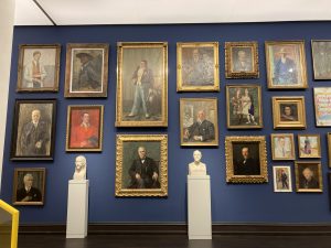 Farbfoto einer Ausstellungswand mit vielen Portraits weißer Männer